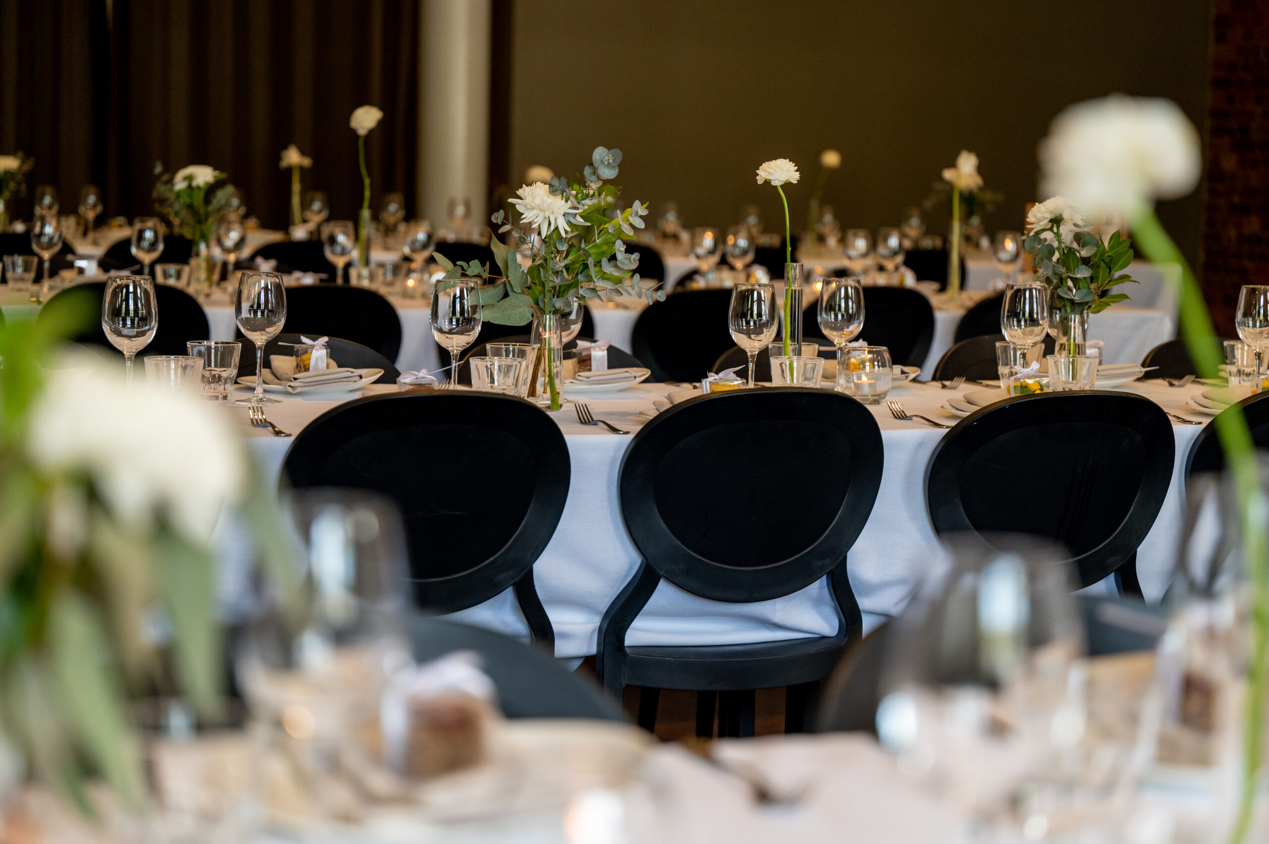 Classic wedding reception tables set with black chairs and floral centrepieces