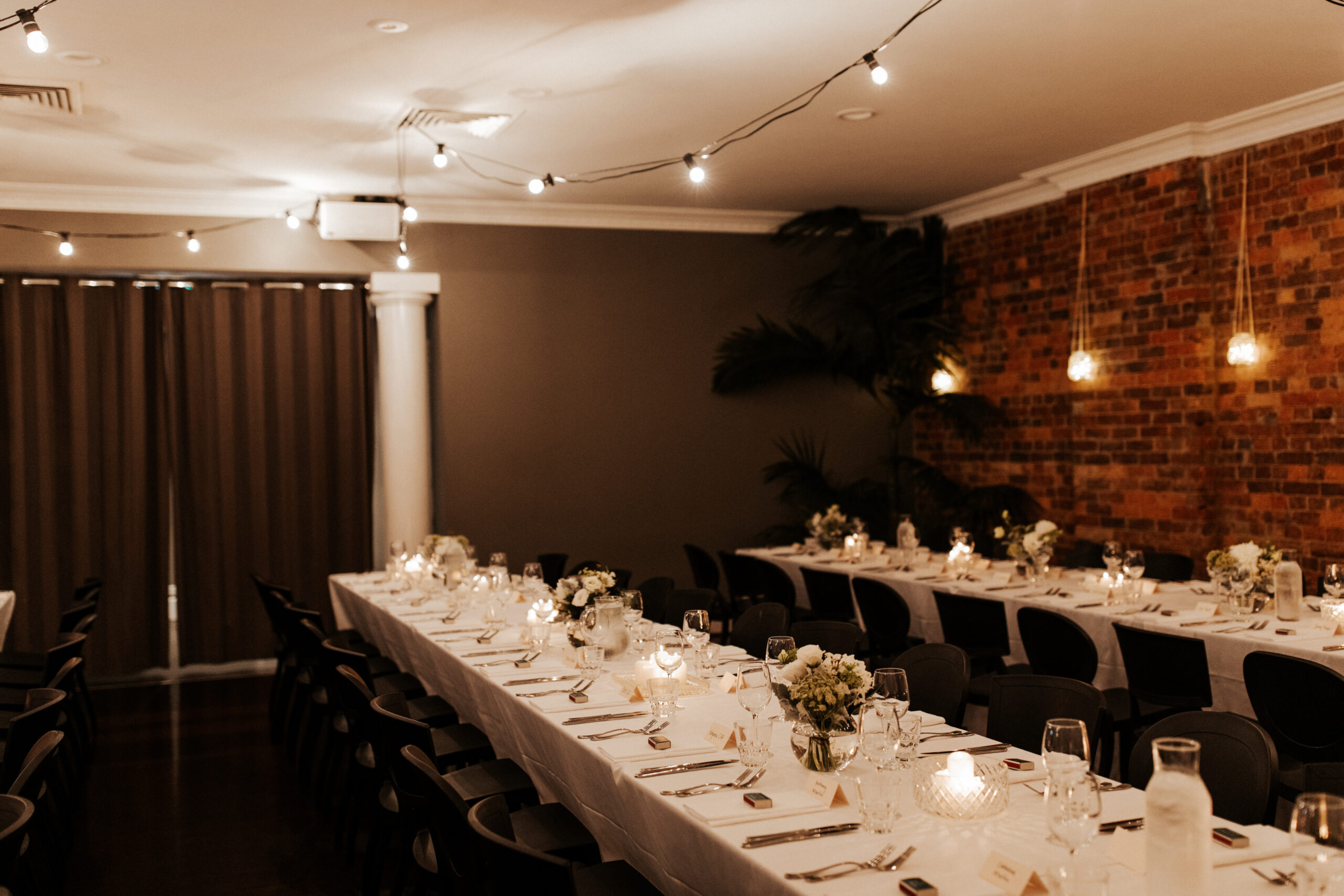 Two long reception tables set with white linen and warm lighting at Transcontinental Hotel